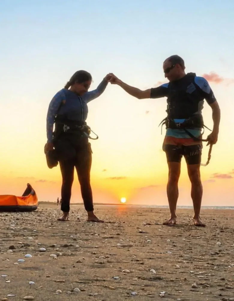 Two kitesurfers walking back along the beach at sunset in Parajuru, Ceará